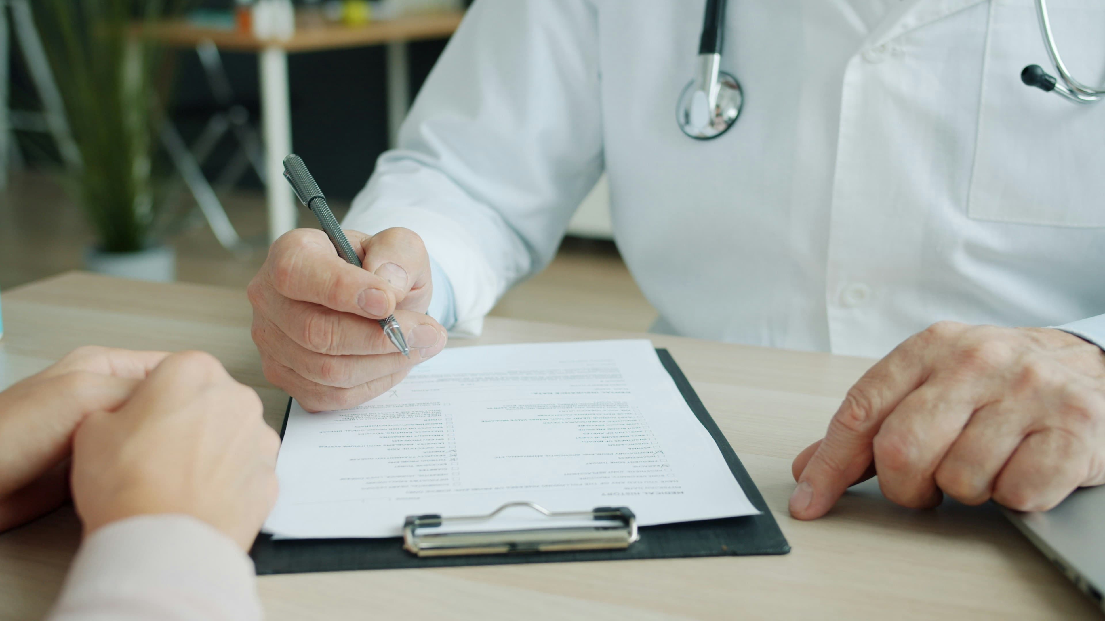 A physician reviewing and signing patient transfer paperwork on a clipboard